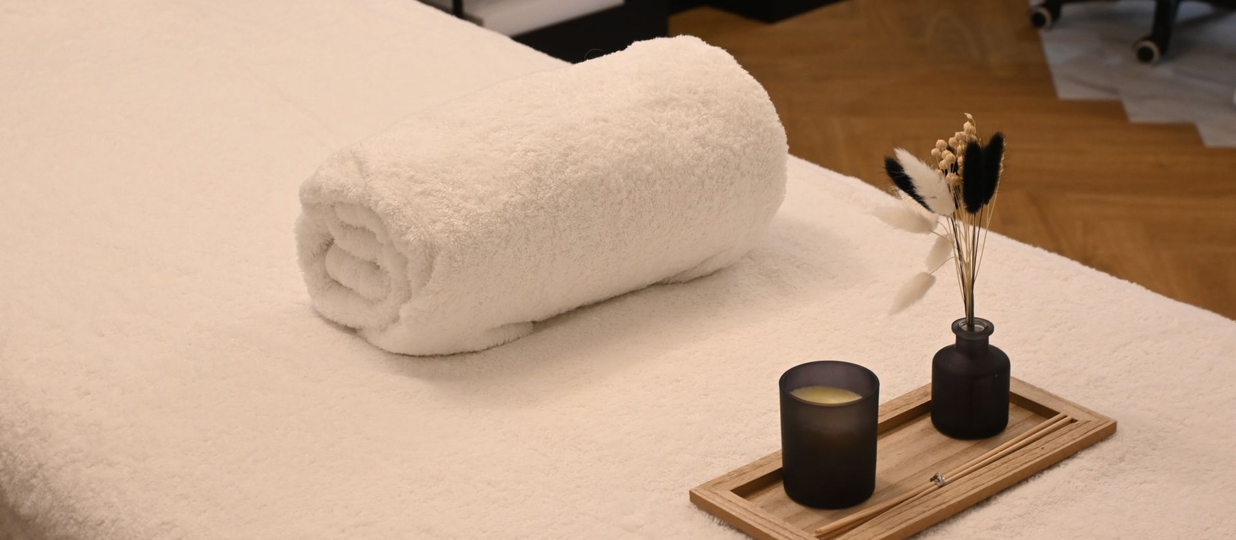Table de massage préparée : linge roulé, bougie et herbes séchées sur un plateau de bois