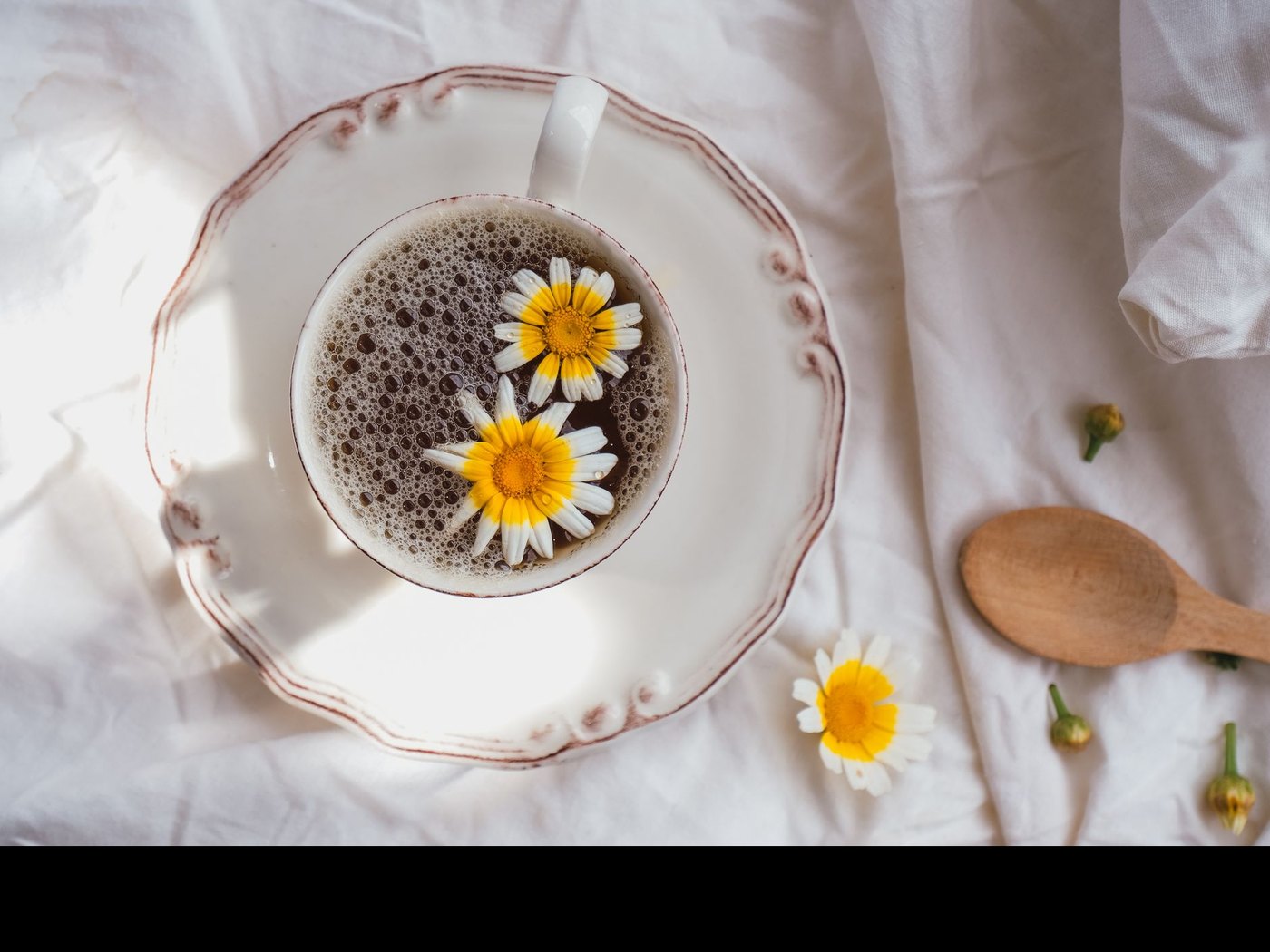 Tasse de tisane et fleurs de camomille posées sur du linge clair